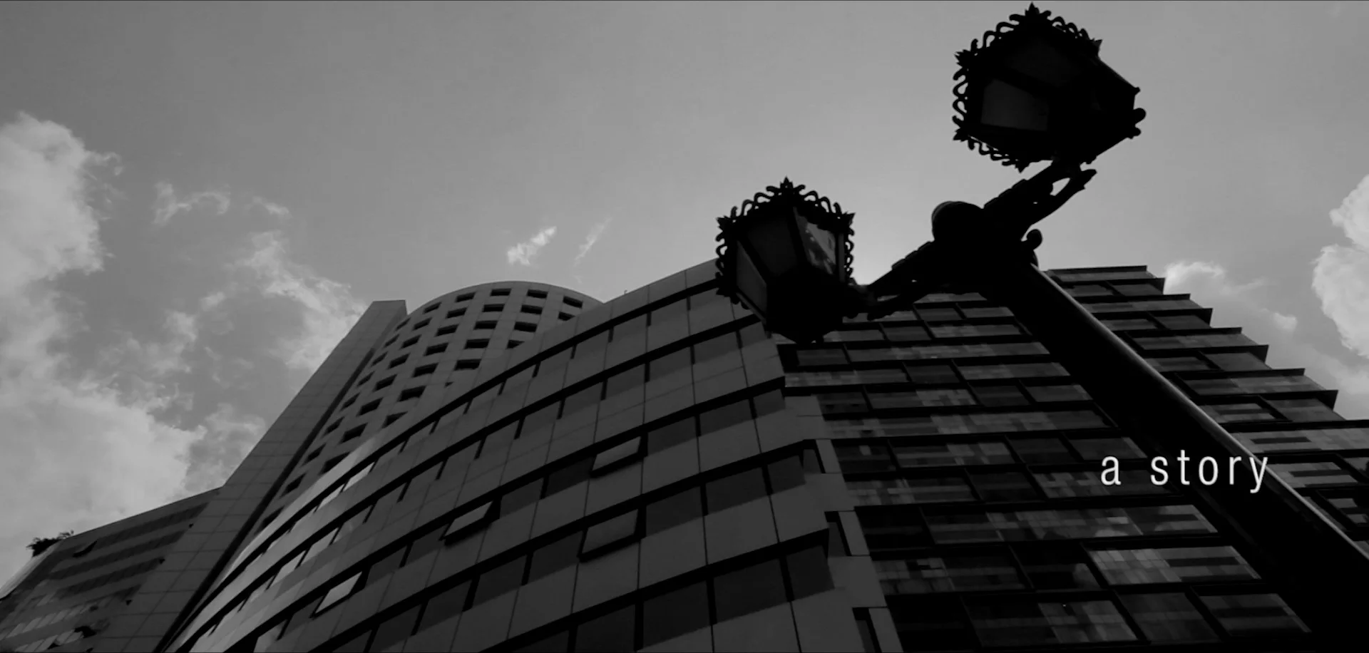 Black-and-white film still of an office tower, opening the story