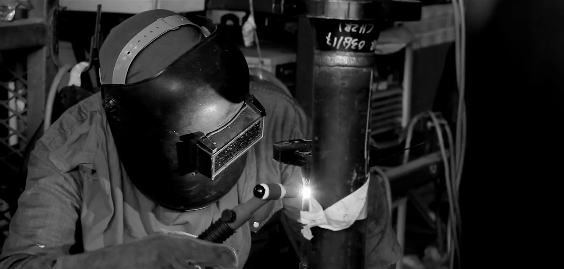 Black-and-white film still of a welder at work in the PESB workshop
