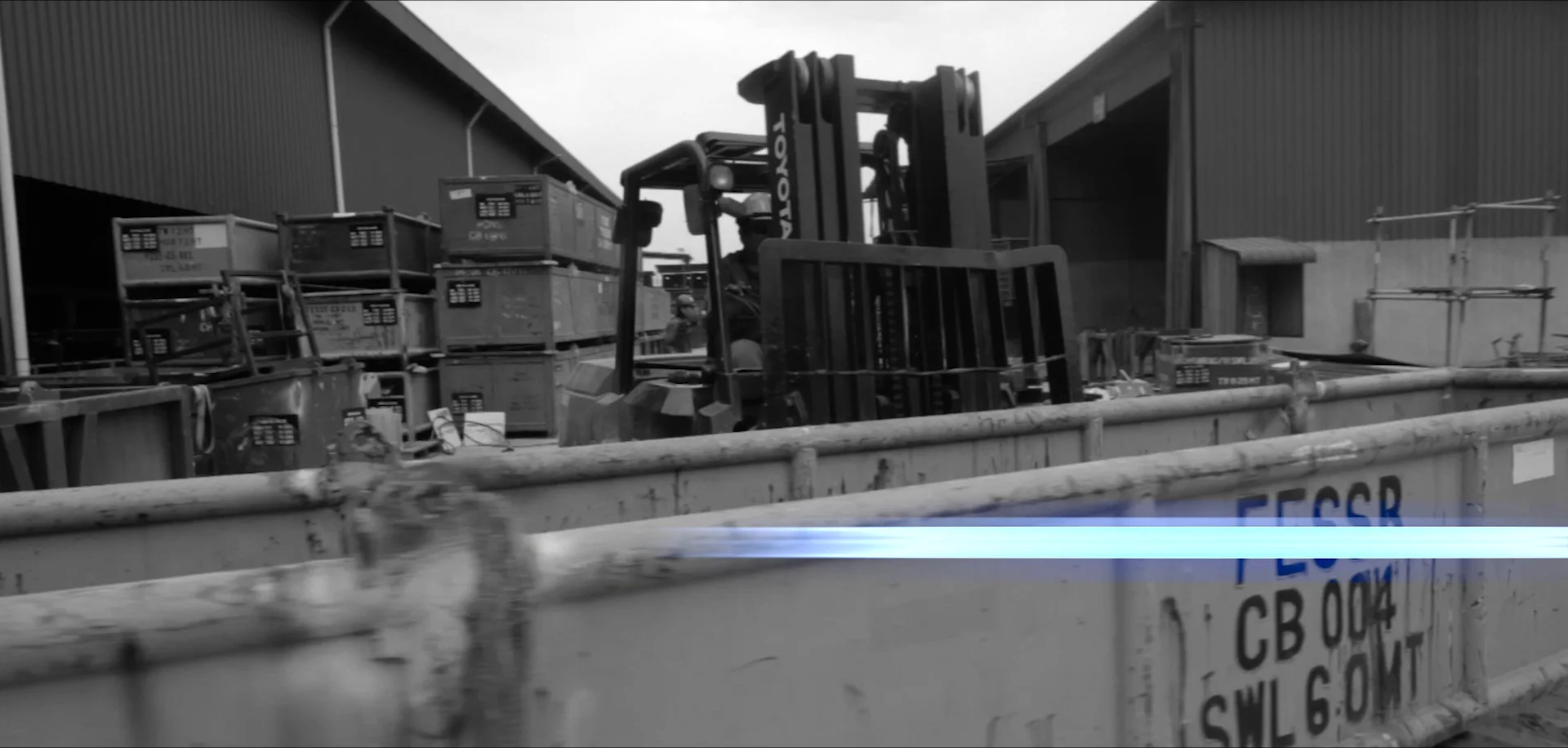 Black-and-white film still of the PESB yard with forklift and steel bins